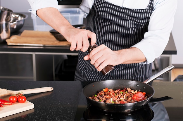 Cuoco unico che prepara i piatti in una padella antiaderente