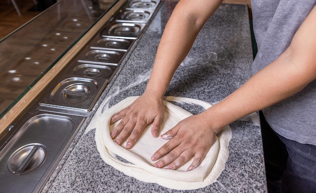 Foto chef che prepara la pasta della pizza a mano la pasta della pizza che viene arrotolata e impastata cuoco