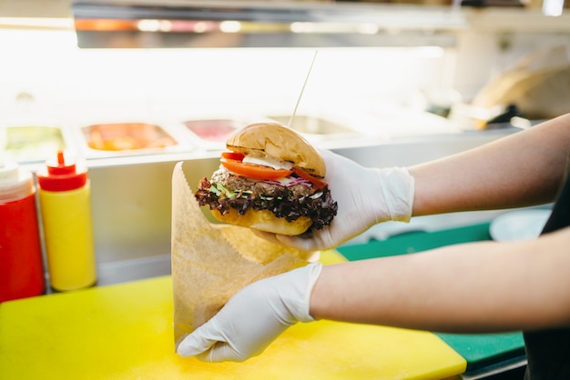 Фото Шеф-повар кладет бургер в картонную упаковку, готовит фаст-фуд. процесс приготовления гамбургера, фастфуд