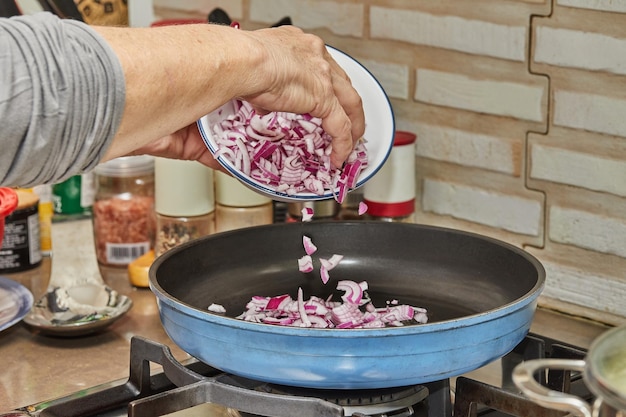 Chef puts purple onions in frying pan on gas stove