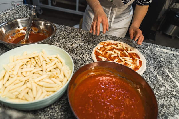 Chef putting penne macaroni and tomato sauce on pizza italian cuisine