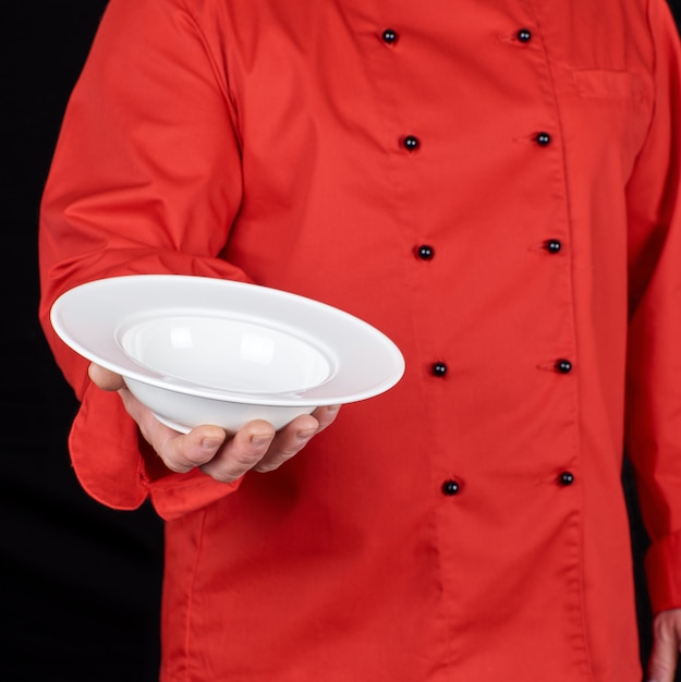 Chef in red uniform holds in his right hand a round white plate for soup