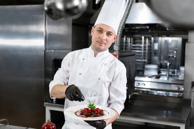 Chef in the restaurant holds a plate with a ready-made dish of meat with strawberries