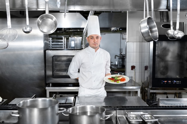 Chef in a restaurant holds a plate with a ready-made dish