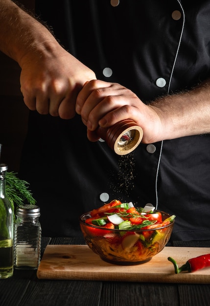 Chef in a restaurant kitchen adds peppers to a fresh vegetable salad