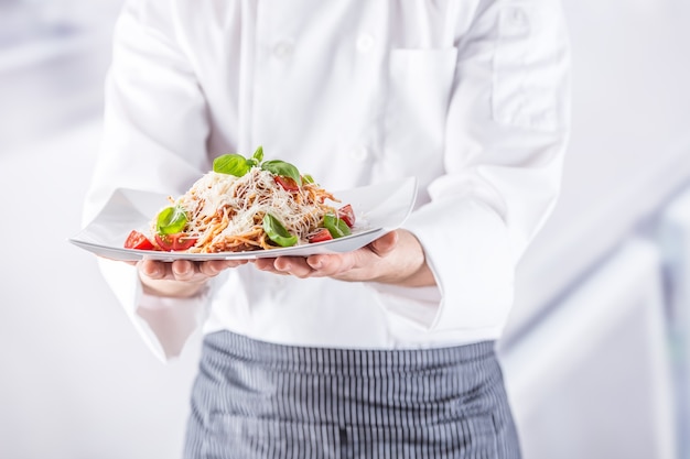 Chef in restaurant kitchen holding plate with italian meal spaghetti bolognese.