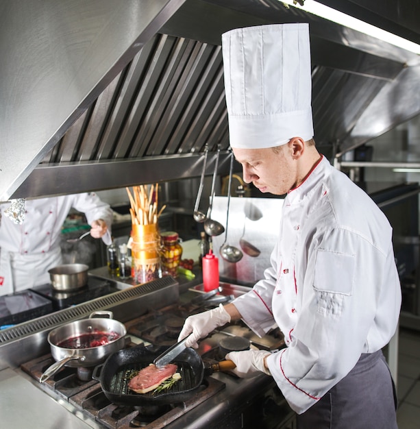 Chef in restaurant kitchen at stove with pan, cooking