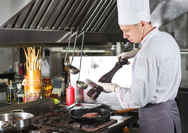 Chef in restaurant kitchen at stove with pan, cooking