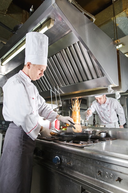 Chef in restaurant kitchen at stove with pan, cooking