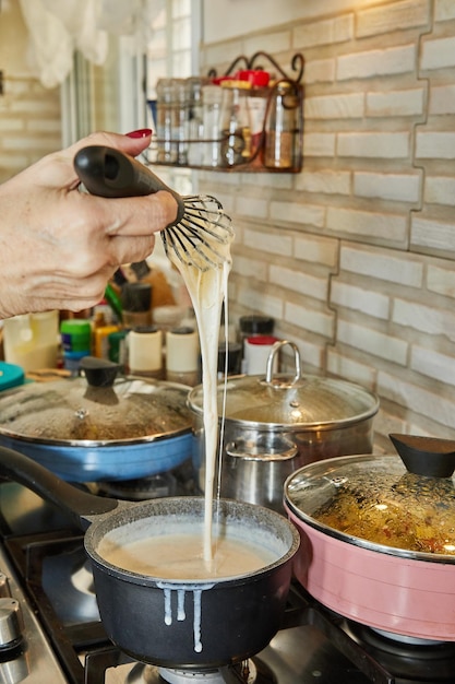 Chef roert de bechamelsaus die wordt gekookt op gasfornuis in pan