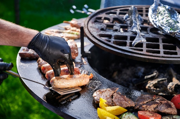 Chef in rubber gloves fries sausages on the grill