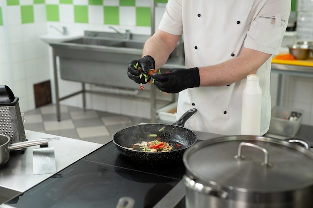 The chef's hand adds sliced vegetables to the pan