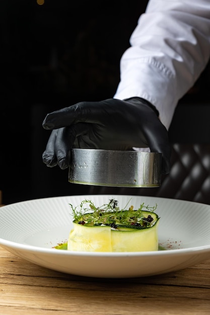 A chef's hand in a black glove reaches for a dish of food.