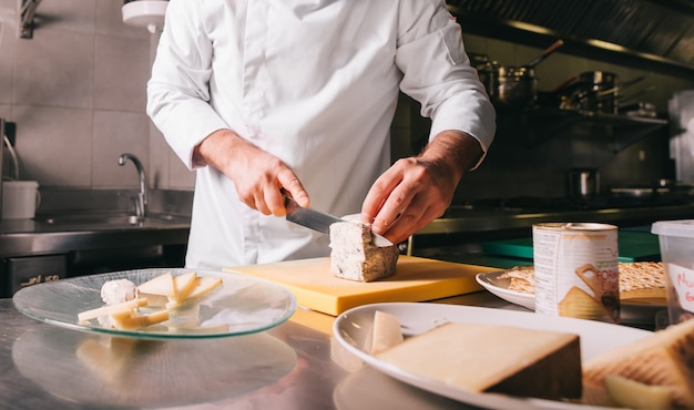 Chef's handen detail tijdens het snijden van kaas op houten snijplank