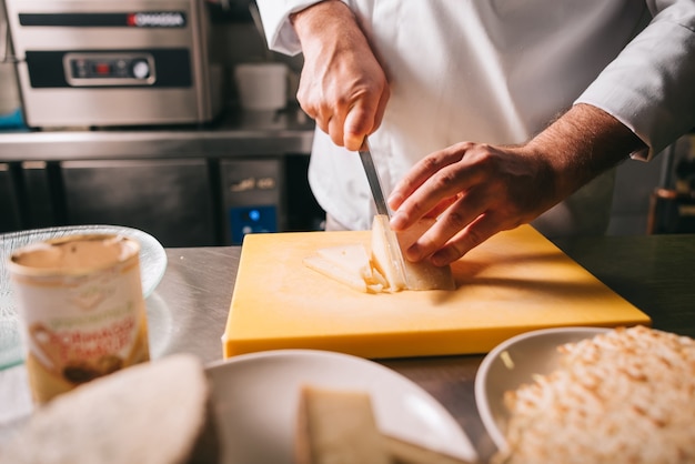 Foto dettaglio delle mani dello chef mentre si affetta il formaggio sul tagliere di legno