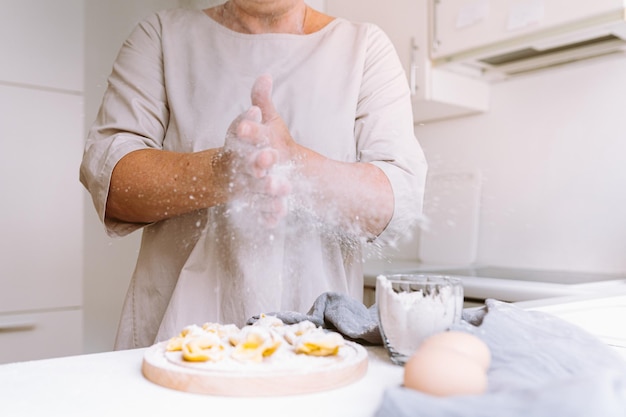 Chef's hands spray flour on dough products. Dumplings, handmade tortellini in home kitchen