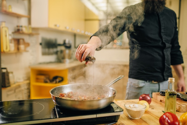 Chef salted meat with vetables into the frying pan