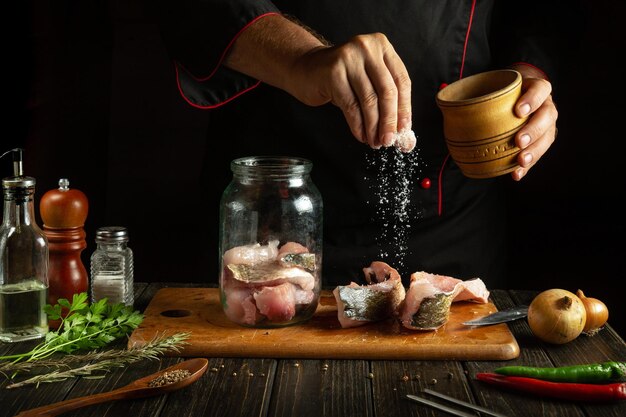 A chef salts steaks with raw fish before cooking herring in a jar Concept of salting or canning fish