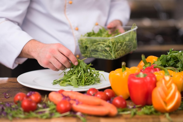 Шеф-повар подает овощной салат на тарелке на кухне ресторана