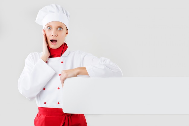 Chef showing blank sign. Woman chef, baker or cook surprise holding blank white paper sign