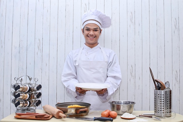 Cuoco unico che mostra piatto vuoto. uomo cuoco o chef che serve piatto vuoto sorridendo felice nel tavolo della cucina