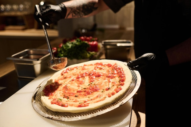 Chef spreading mixture of ingredients on surface of pizza flatbread