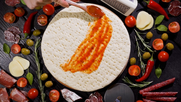 Foto lo chef spalma la salsa di pomodoro sull'impasto della pizza nel ristorante pizzeria