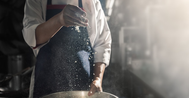 Chef sprinkles the flour to cook in kitchen