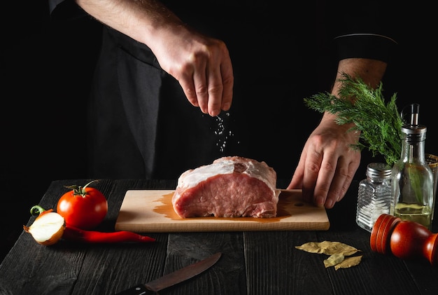 The chef sprinkles the meat with salt. Preparing meat before baking. Working environment in the kitchen of a restaurant or cafe