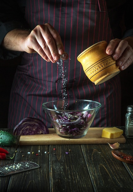 Chef sprinkles salt on a fresh red cabbage salad in a restaurant kitchen