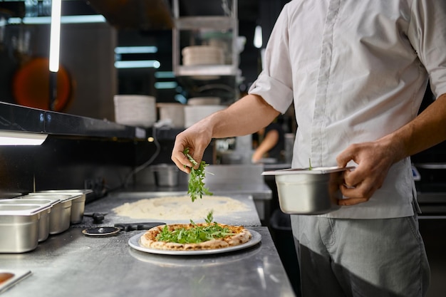 Chef sprinkling fresh greenery over traditionally made pizza. Italian fast food restaurant