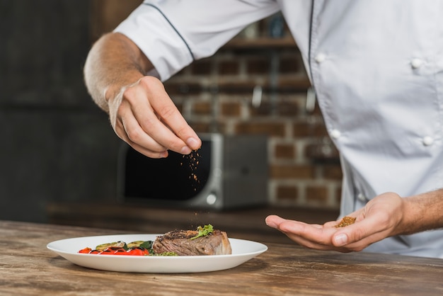 Photo chef sprinkling spices over the prepared dish