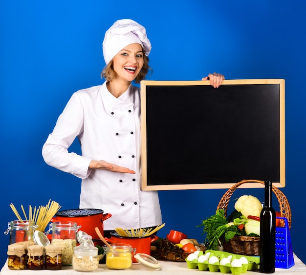 Chef staat aan tafel met een bos groente houdt een zwart bord vast voor reclame voor een gezond dieet