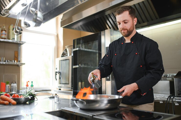 Photo chef standing in restaurant and making flambe on frying pan