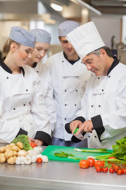 Foto chef che insegna ai tirocinanti come tagliare le verdure