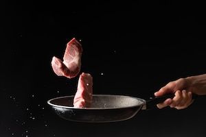 Chef tossed up fresh pork or beef steak frozen in the air on a black background