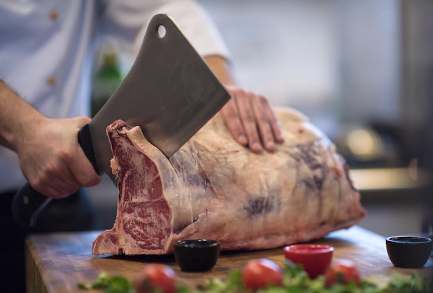 chef using ax while cutting big piece of beef  on wooden board in restaurant kitchen