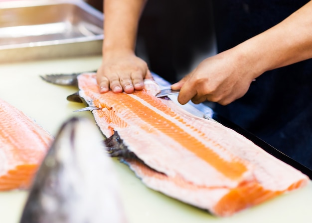 Шеф-повар использует нож для нарезки филе лосося, шеф-повар нарезает лосося в ресторане