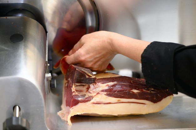 Foto chef indossa utilizzando la macchina per affettatrice di prosciutto