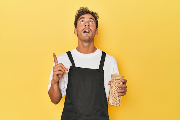 Chef with chickpeas jar on yellow pointing upside with opened mouth