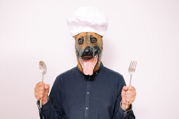 Шеф-повар с маской собаки показывает ложку и вилку для еды