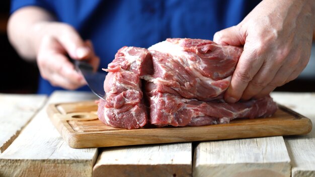 A chef with a knife cuts a raw pork neck.