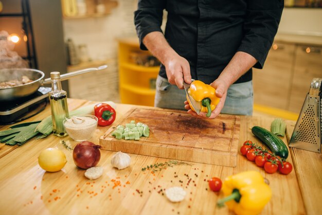 Photo chef with knife cuts yellow pepper on wooden board