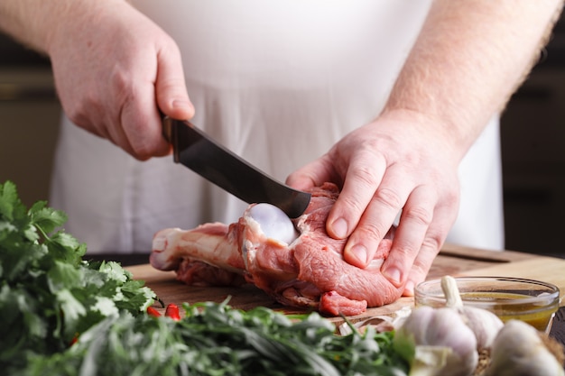 Chef with a knife in their hand cuts fresh meat on a table