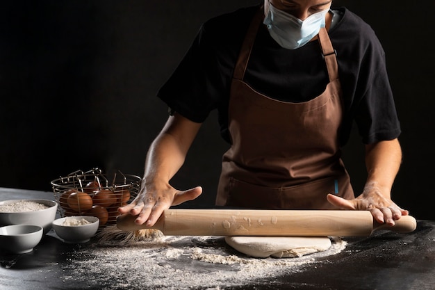 Chef with medical mask rolling dough on the table
