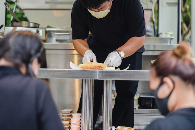 Chef with protective mask preparing sandwich on food truck.