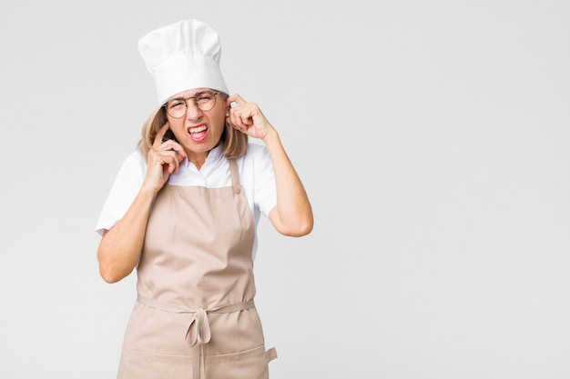 chef woman covering both ears to a deafening noise sound or loud music