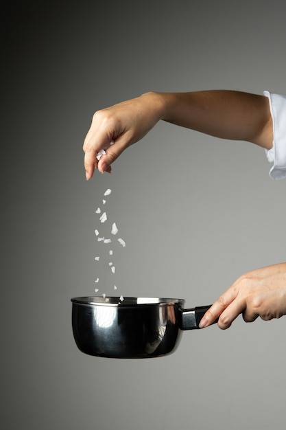 Chef woman sprinkle salt cooking prepare food seasoning on grey background 