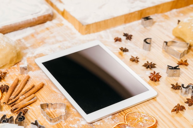 Foto tablet sul posto di lavoro dello chef con schermo mockup nero su un tavolo di legno ricoperto di farina e spezie