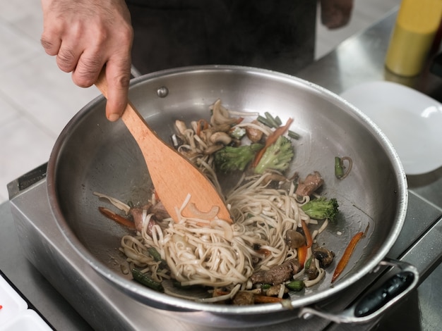 シェフはレストランの厨房で働いています。男性料理人がフライパンで食事を準備しています